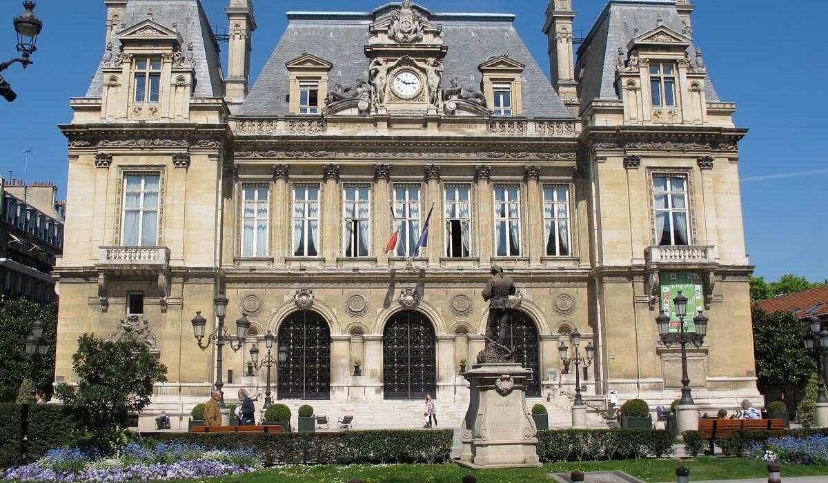 Hôtel de ville historique avec jardin fleuri en été.