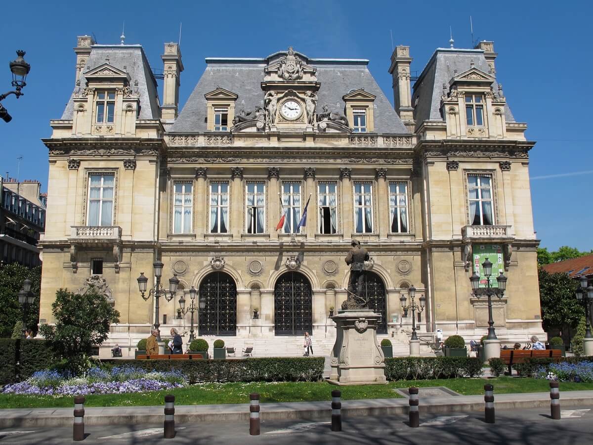Hôtel de ville historique avec jardin fleuri en été.