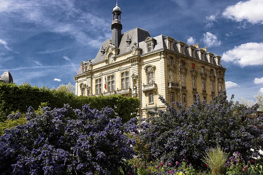 Hôtel de ville entouré de fleurs violettes sous ciel bleu.