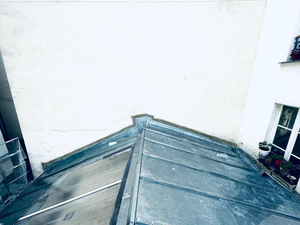 Toiture en zinc avec mur blanc et fenêtre.