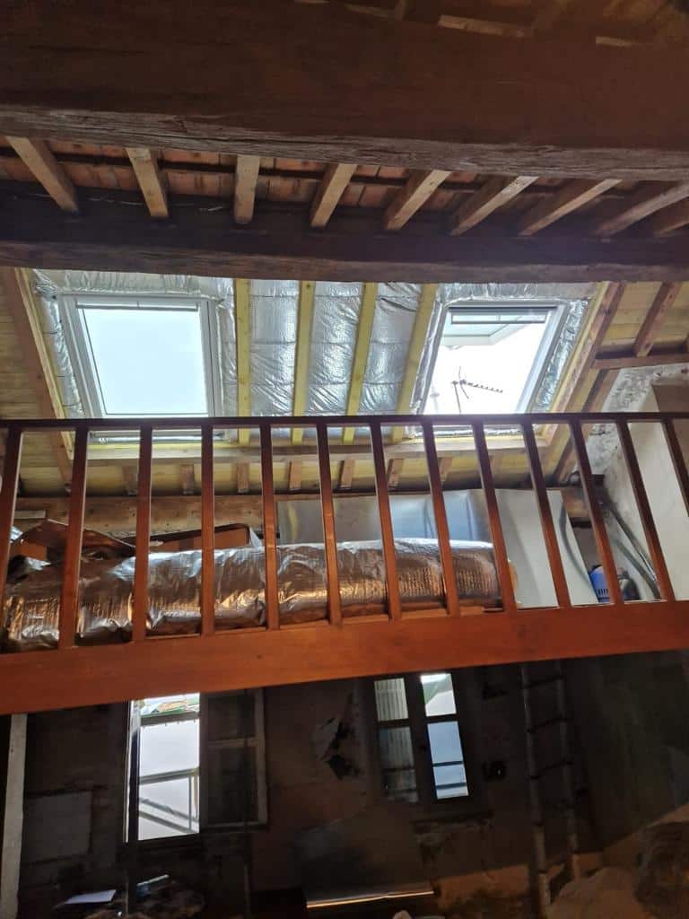 Grenier en rénovation avec charpente et fenêtres de toit.