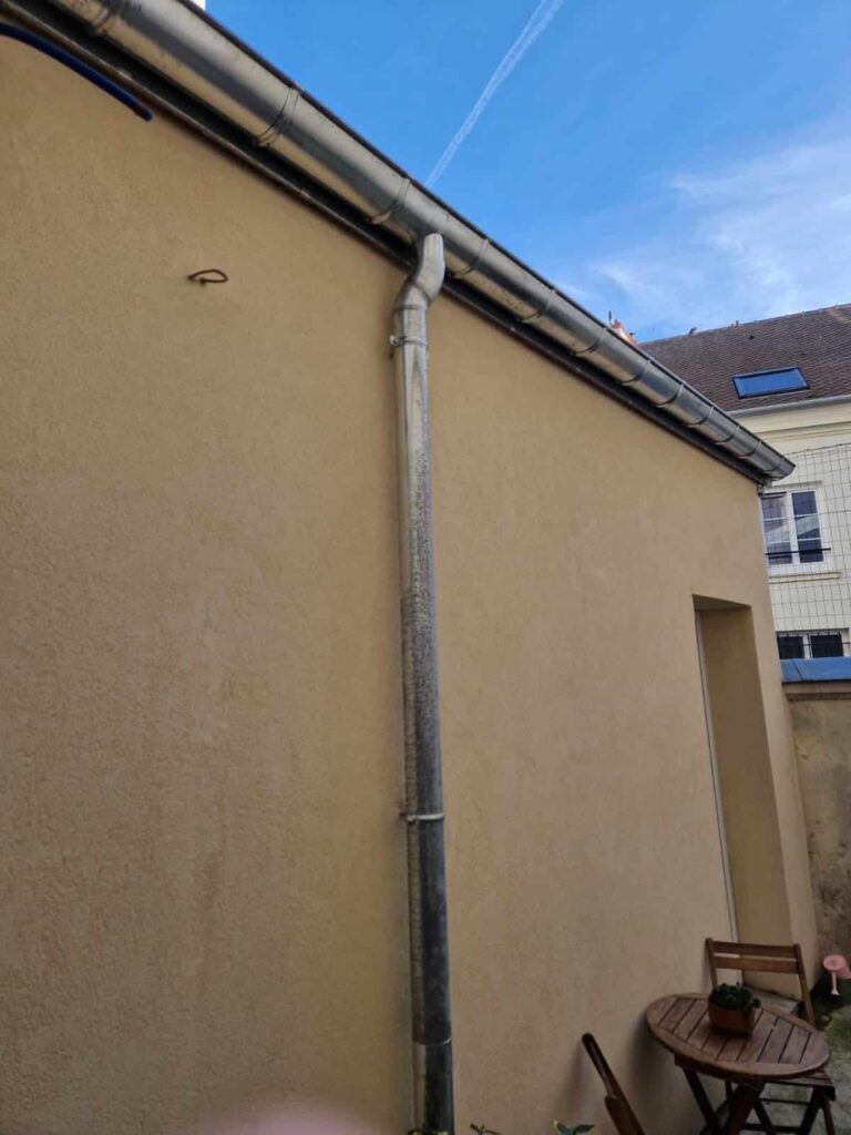 Façade avec gouttière et mobilier de jardin.